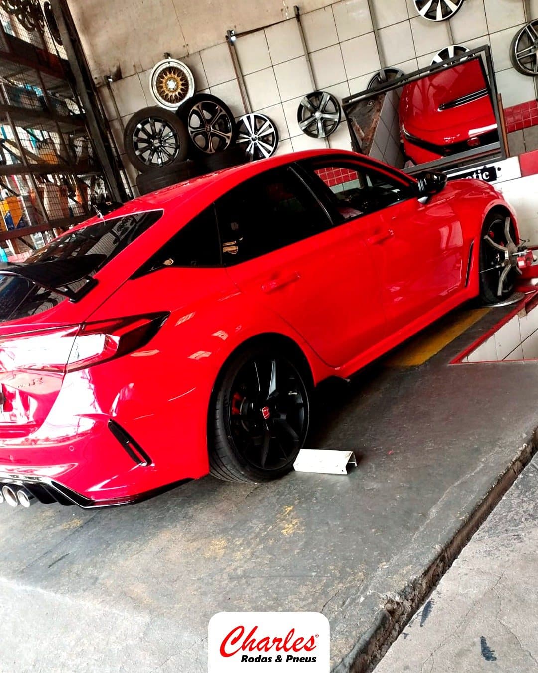 Carro esportivo vermelho na oficina, ao lado da parede de rodas